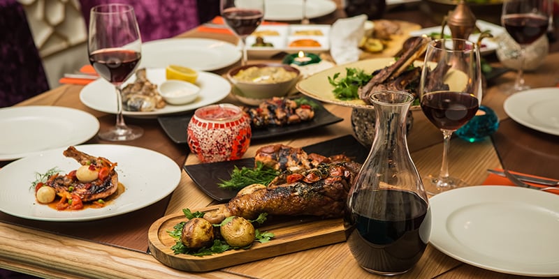 Tavolo imbandito per pranzo con piatti contenti carne e calici con vino rosso