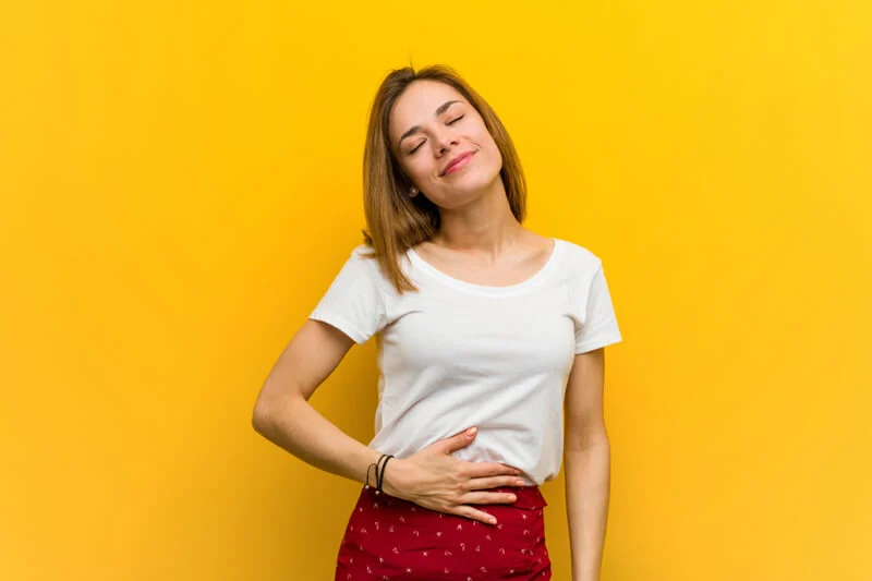 Ragazza che si accarezza la pancia sorridendo su uno sfondo giallo