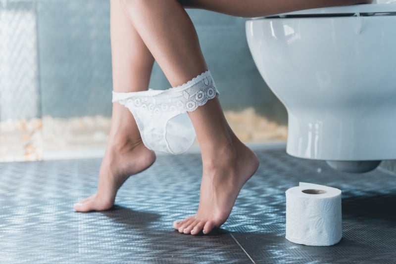 Dettaglio di gambe femminili di una donna seduta sul WC