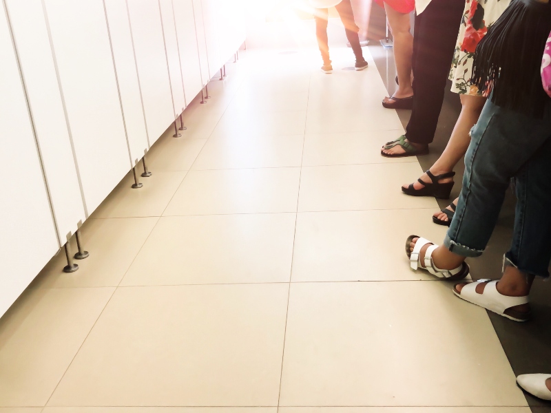 Dettaglio di gambe femminili in fila ai bagni pubblici