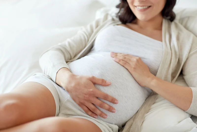 Donna in gravidanza distesa su un letto con le mani sulla pancia