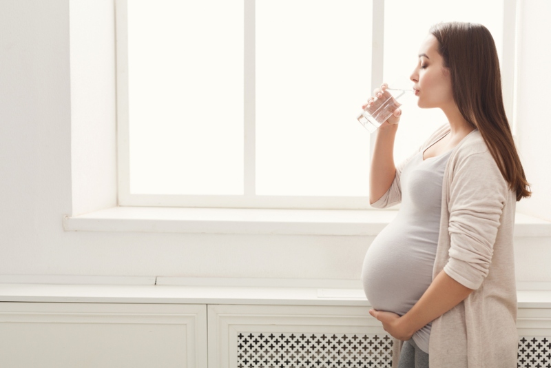 Donna in gravidanza che beve accanto ad una finestra