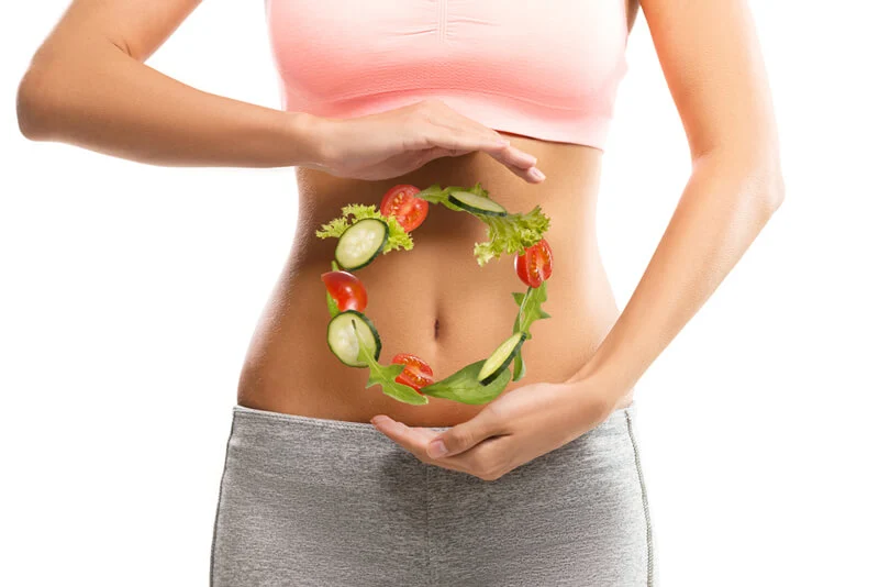 Dettaglio di una pancia femminile su cui le mani disegnano un cerchio in cui sono presenti gli alimenti per una dieta sana: verdura e pomodori