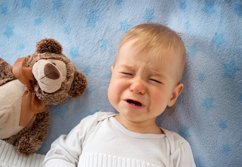 Bambino piccolo che piange accanto ad un orsacchiotto di peluche