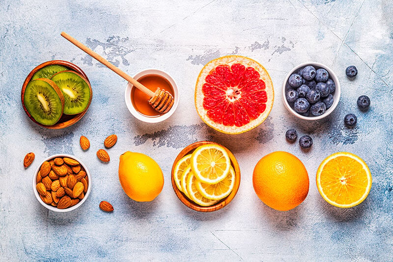 Ciotole con cibi sani su un tavolo: kiwi, miele, arancia rossa, mirtilli, mandorle, limone e arancia